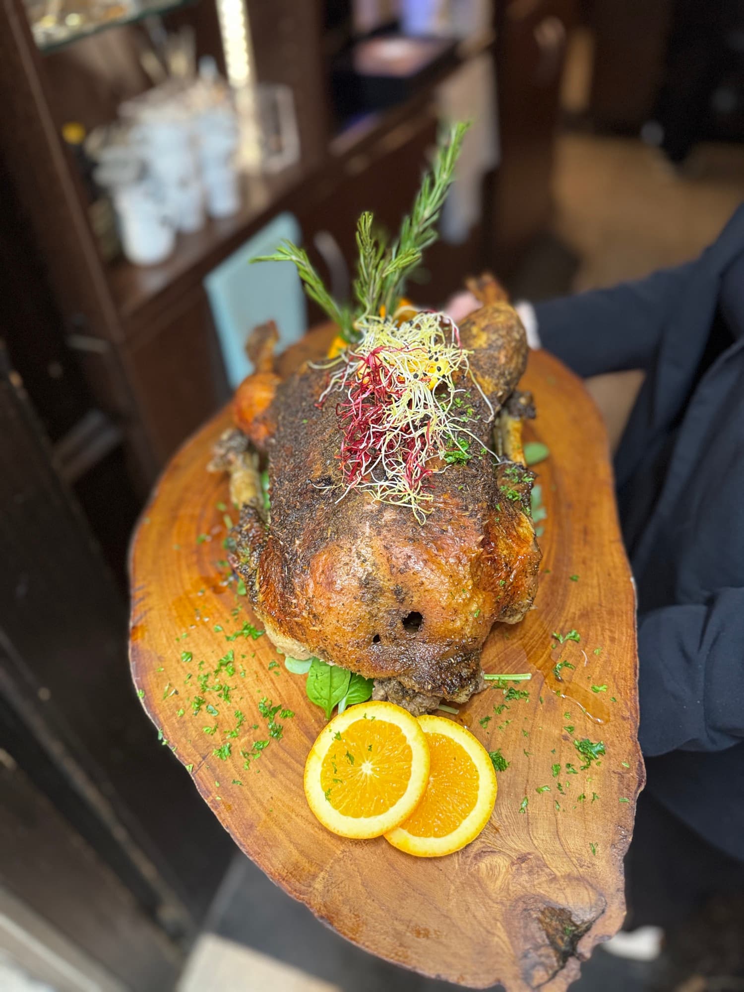 Ganze gebratene Gans auf einem Holzbrett, mit Rosmarin und Orangenscheiben angerichtet