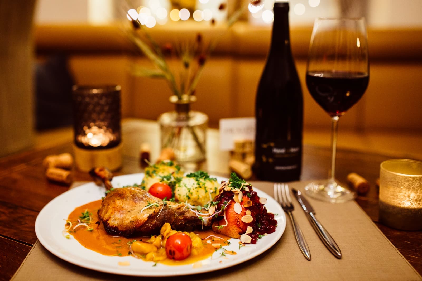 Gänsekeule mit Kartoffelklößen, Apfelrotkohl und Bratapfel auf dem Teller, dazu ein Glas Rotwein